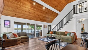 A spacious living area with a high ceiling, wooden flooring, and a staircase leading to an upper level.