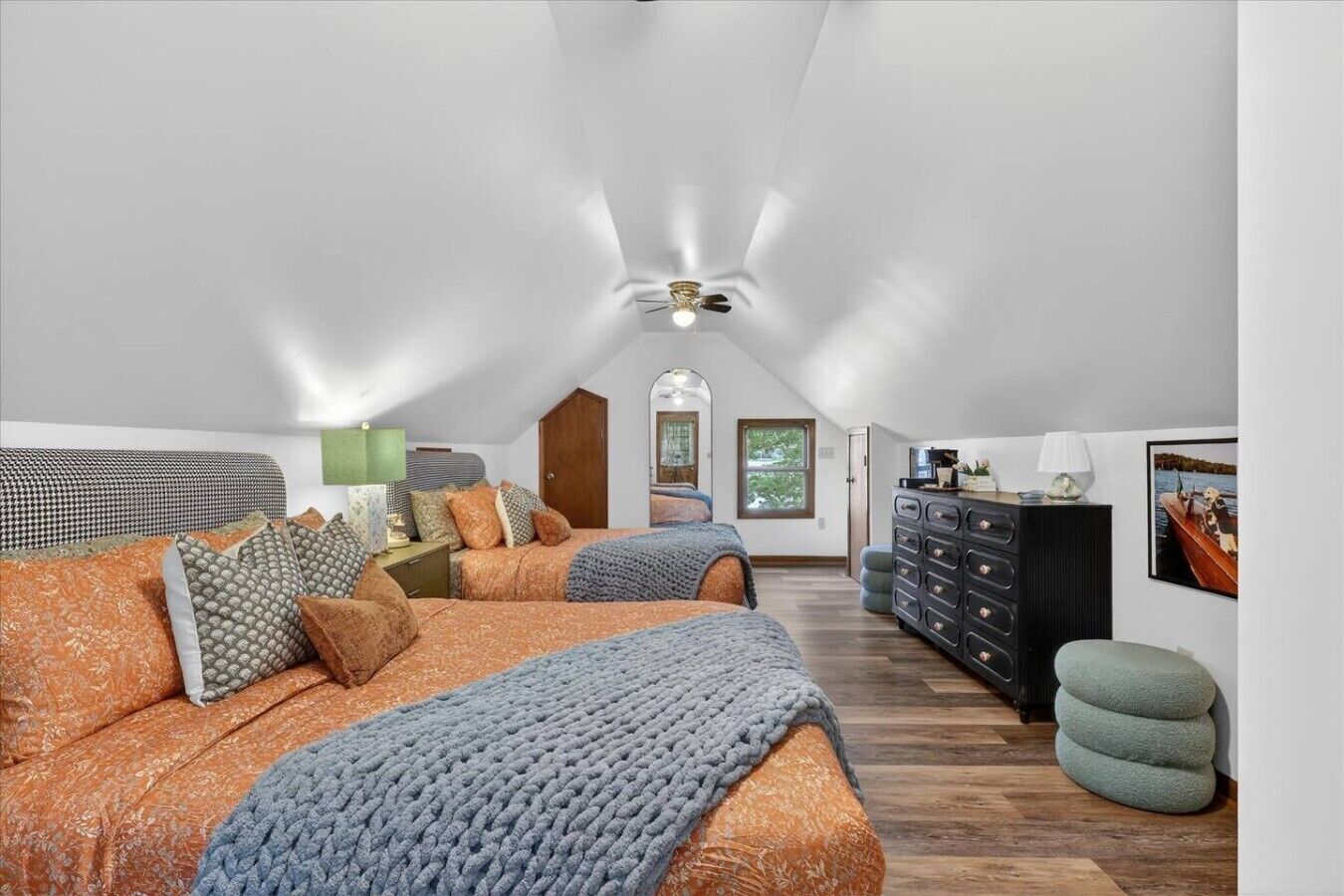 Een ruime zolderkamer met een hoge nok, een groot bed, een kast en een raam met uitzicht.