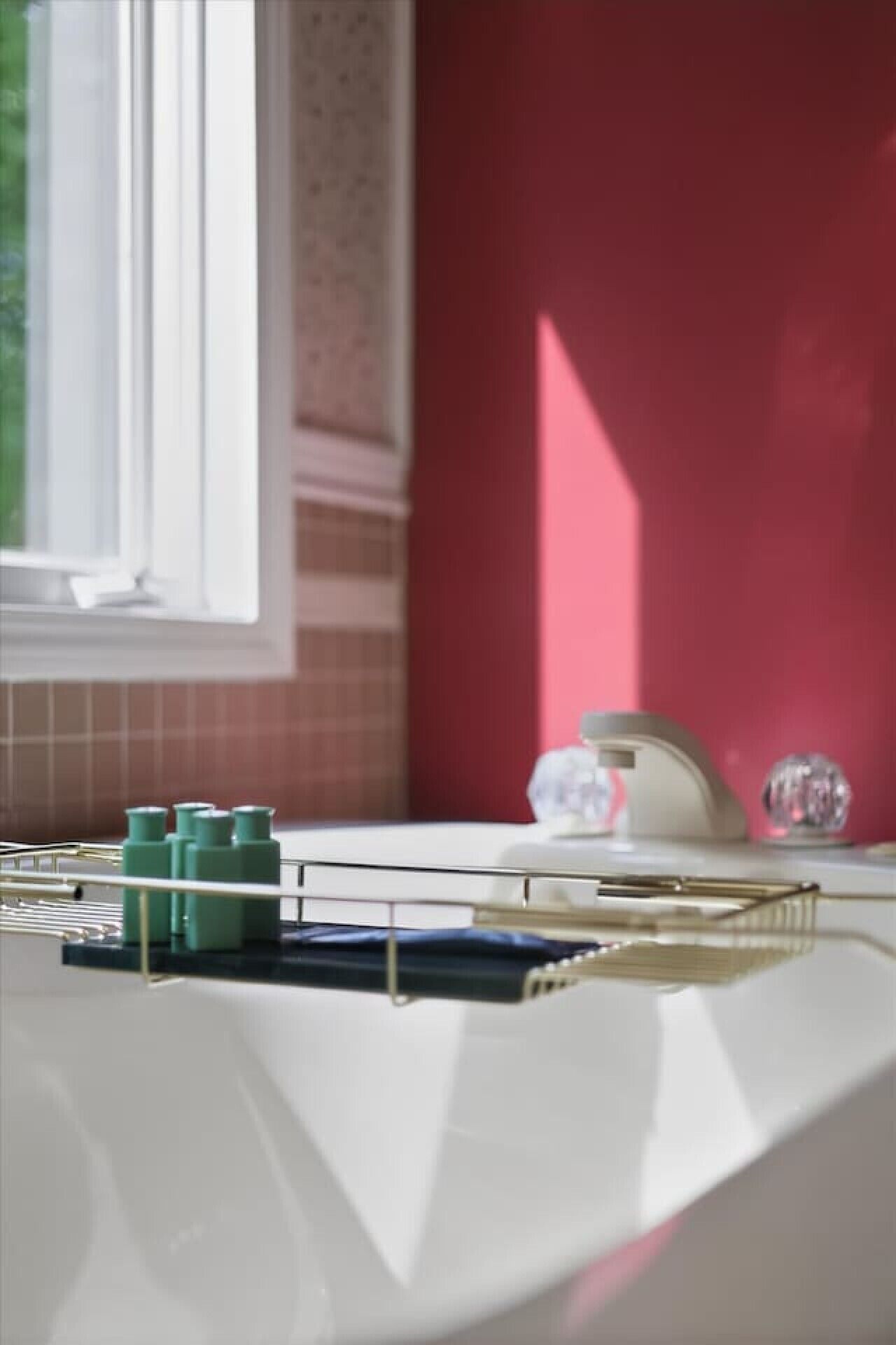 Un plan de travail de cuisine avec un évier blanc, une fenêtre et un mur rouge.
