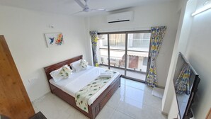 A hotel room with a bed, a television, a ceiling fan, a window with curtains, and an air conditioning unit. - Elis Hospitality Service Private Limited (Sanand)
