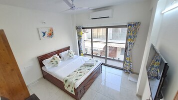 A hotel room with a bed, a television, a ceiling fan, a window with curtains, and an air conditioning unit.