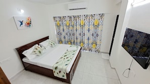 Un dormitorio con una cama, un televisor, una cortina estampada y un aire acondicionado instalado en la pared.