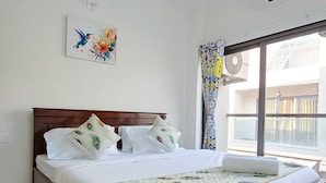 A bedroom with a wooden bed, a ceiling fan, a window with curtains, and a wall-mounted air conditioning unit. - Elis Hospitality Service Private Limited (Sanand)