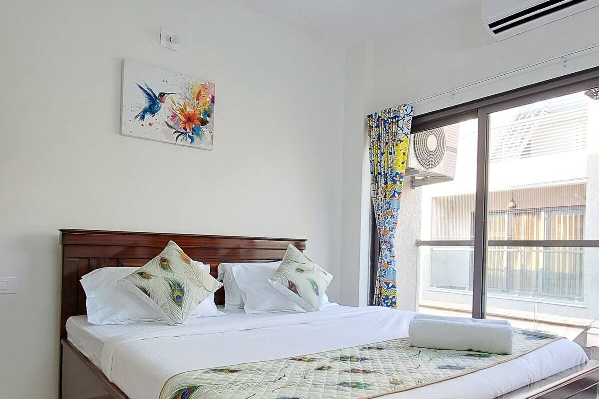 Un dormitorio con cama de madera, ventilador de techo, ventana con cortinas y aire acondicionado instalado en la pared.