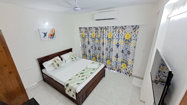 Un dormitorio con cama, ventilador de techo, aire acondicionado y cortina con estampado floral.