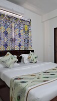 Una habitación de hotel con cama, almohadas y cortina con diseño colorido.