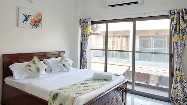 A bedroom with a bed, ceiling fan, air conditioning unit, and a view of the outside. - Elis Hospitality Service Private Limited (Sanand)