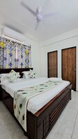 A bedroom with a bed, a ceiling fan, patterned curtains, and wooden doors.