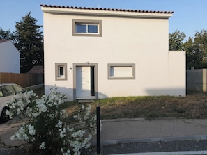 A two-story building with a white facade, a small window on the upper floor, and a door with a glass panel.