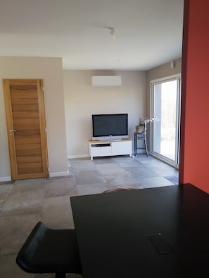 A room with a TV, a wooden door, a white cabinet, and a large window.