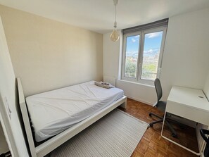Une chambre avec un lit simple, un bureau et une fenêtre donnant sur la ville.