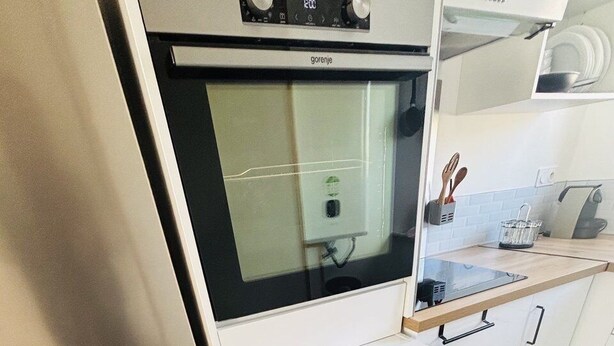 Una cucina con frigorifero in acciaio inossidabile, mobili bianchi, piano di lavoro in legno e pavimento piastrellato.