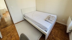 Una stanza piccola e pulita con un letto singolo, una sedia, un termosifone e una lampada a sospensione.