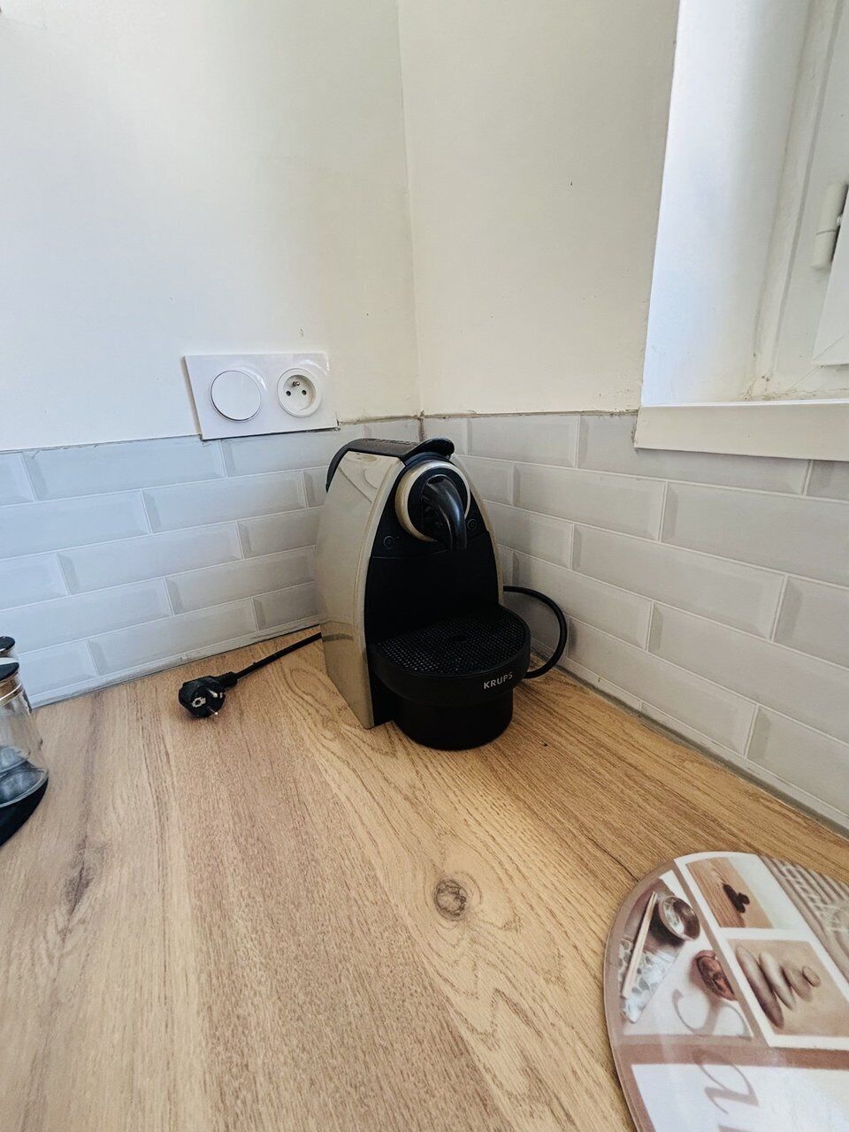 A small kitchen with a coffee machine, a power outlet, and a wooden floor.