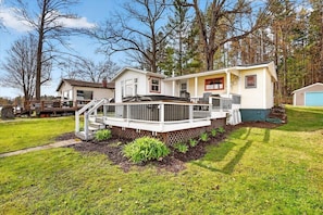 A two-story house with a deck, a garage, and a yard with grass and trees.