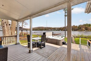 A covered deck with a hot tub, outdoor seating, and a view of a lake.