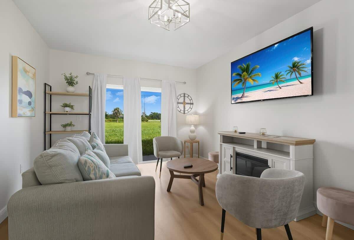 A modern living room with a sofa, chairs, a fireplace, and a TV displaying a beach scene.