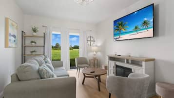 A modern living room with a sofa, chairs, a fireplace, and a TV displaying a beach scene.