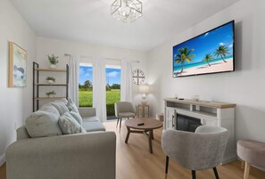 A modern living room with a sofa, chairs, a fireplace, and a TV displaying a beach scene. - Chic 3BR, 2BA – Brand New! (Englewood)