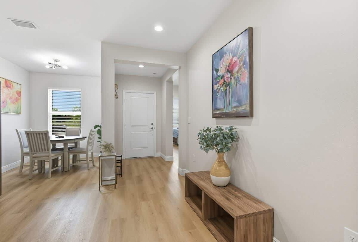 A well-lit hallway with a dining area, a door leading to another room, and a painting on the wall.