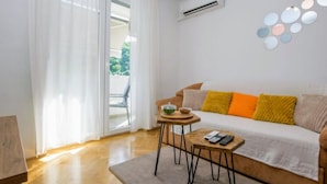 A modern living room with a sofa, a small table, and a view through a glass door. - Comfort Apartment Dea (Rijeka)