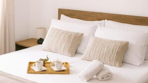 A neatly made bed with white linens and beige pillows, a wooden headboard, a bedside table with a lamp, and a tray with cups and a rolled towel. - Comfort Apartment Dea (Rijeka)