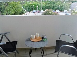 En balkon med et bord, stole og udsigt over en parkeringsplads og træer.