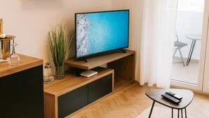 A modern living room with a flat-screen TV, wooden furniture, and a glass door leading to a balcony. - Comfort Apartment Dea (Rijeka)