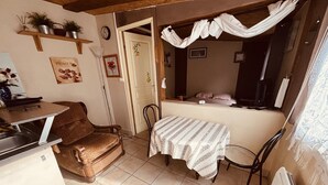 A compact kitchen with a dining area, a small table with a patterned tablecloth, a chair, and a radiator.