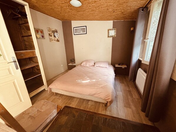 A bedroom with a bed, a wardrobe, a bedside table, a radiator, and a window with curtains.