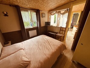 A bedroom with a bed, a desk, a chair, a radiator, and a window with curtains. - The 6th of the Cressonnière (Agny)