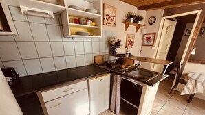 A compact kitchen with white cabinets, a black countertop, a sink, and a dining area with a chair.