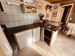 A compact kitchen with white cabinets, a black countertop, a sink, and a dining area with a chair. - The 6th of the Cressonnière (Agny)