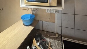 A kitchen with a microwave on a shelf, a blue bowl, and various kitchen utensils.