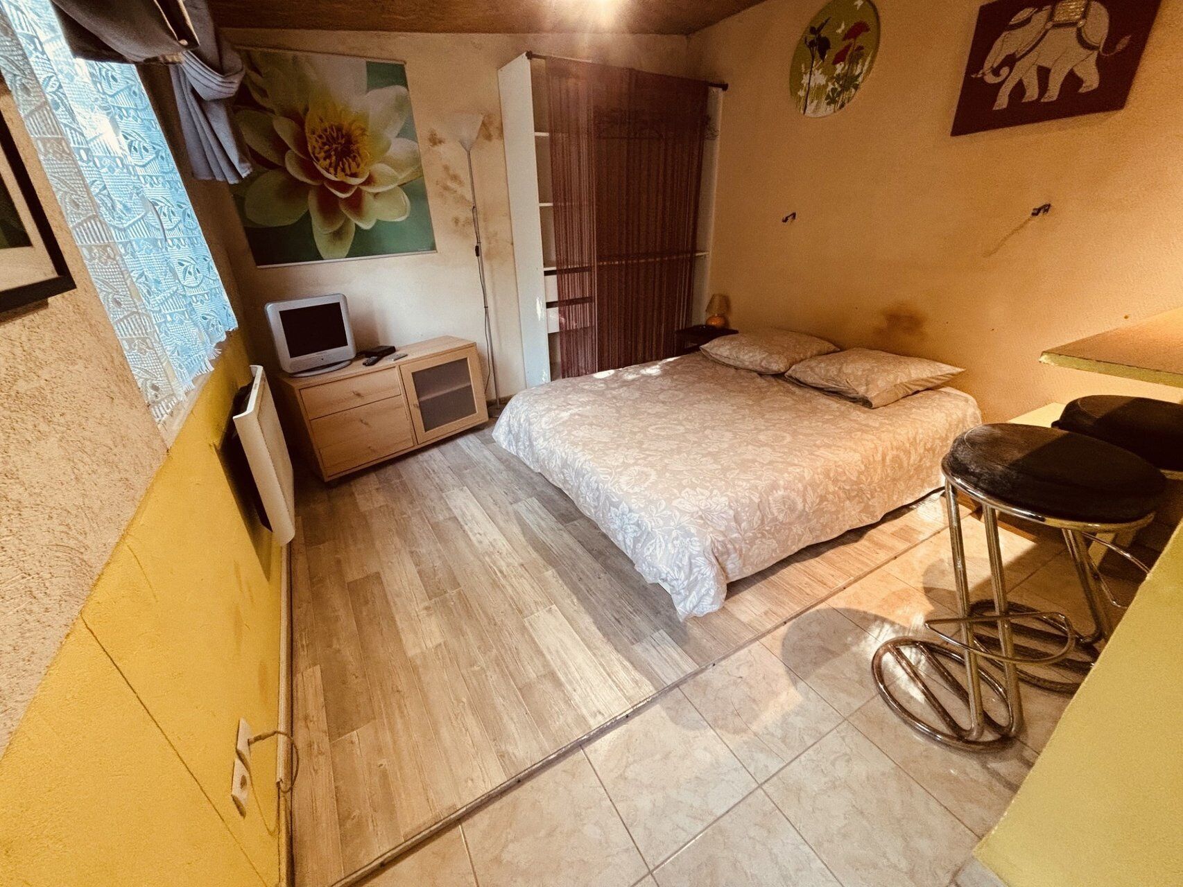 A bedroom with a bed, a TV, a wardrobe, and a stool.