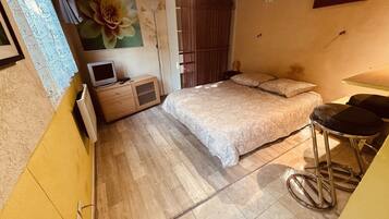 A bedroom with a bed, a TV, a wardrobe, and a stool.