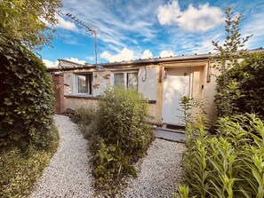 Un petit bâtiment avec un chemin de gravier, entouré de verdure et sous un ciel dégagé.