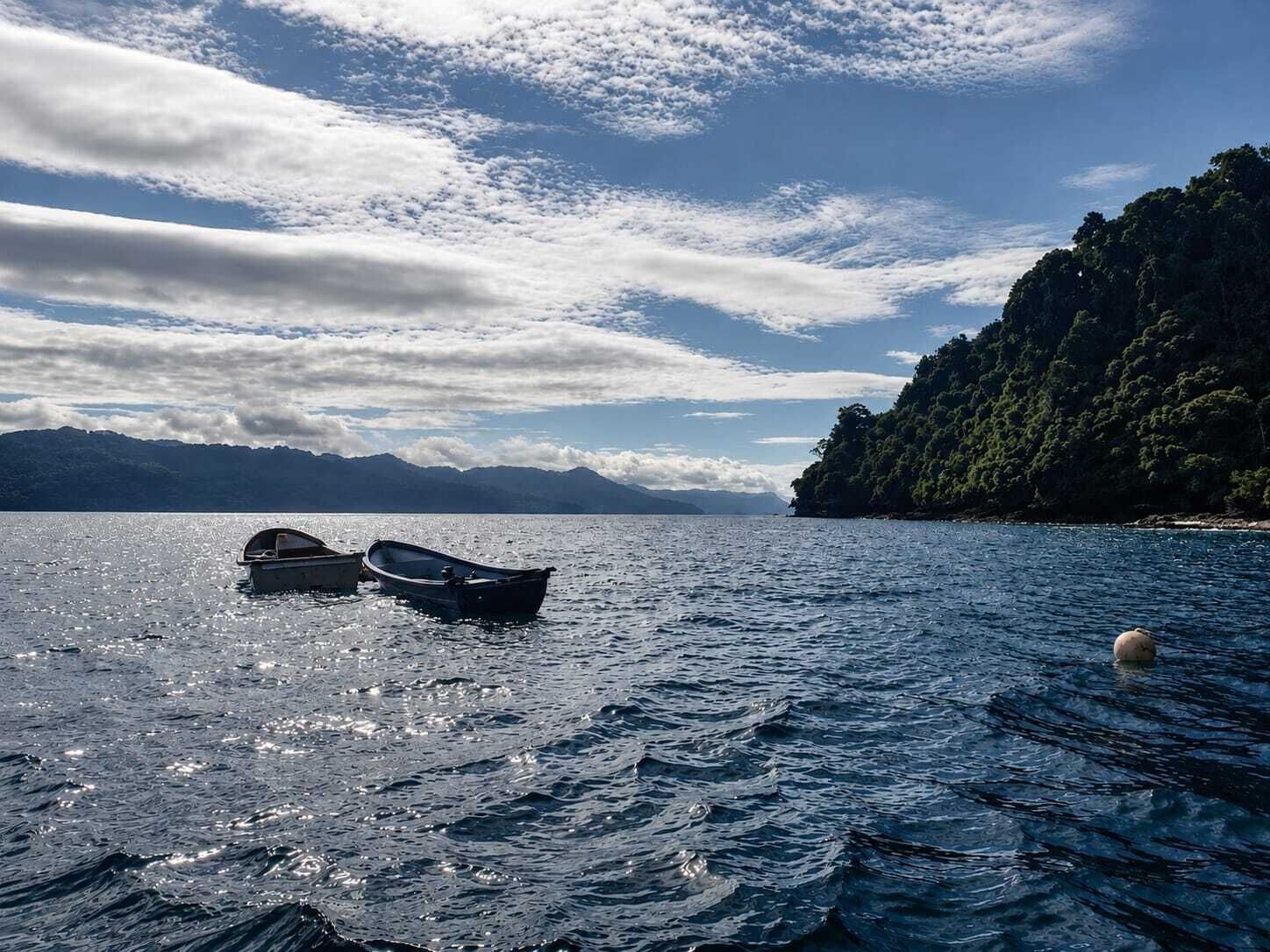 A calm lake with boats, a buoy, and a forested cliff.