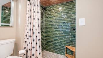 A bathroom with a shower curtain featuring star patterns, a green-tiled wall, a wooden bench, and a white toilet.