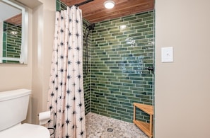 A bathroom with a shower curtain featuring star patterns, a green-tiled wall, a wooden bench, and a white toilet.