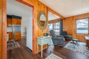 A wooden interior with a kitchen, a dining area, and a large window offering a view.