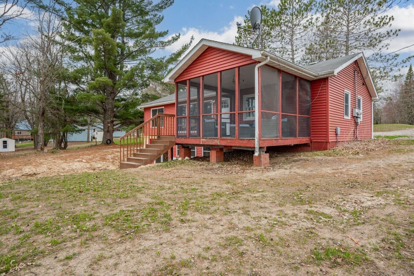 Une maison en bois rouge avec une véranda grillagée et un petit escalier menant à l’entrée.
