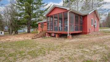 Une maison en bois rouge avec une véranda grillagée et un petit escalier menant à l’entrée.