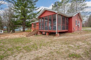 A red wooden house with a screened porch and a small staircase leading to the entrance.