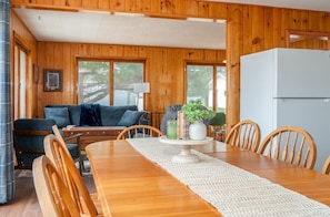 A wooden interior with a dining table, chairs, a sofa, and a refrigerator.