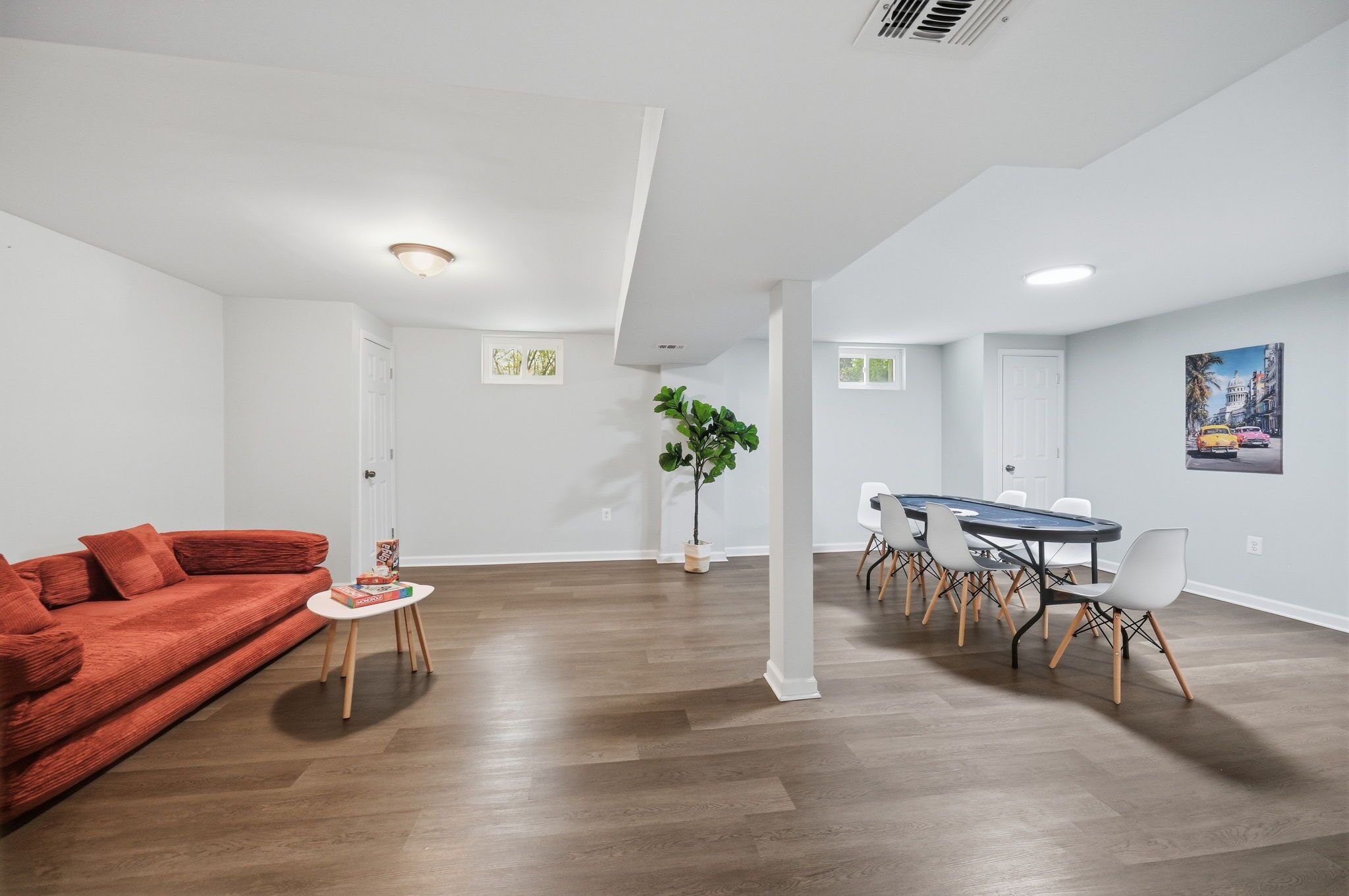 Un salon moderne avec un canapé rouge, une petite table, un coin repas avec une table bleue et des chaises blanches, et une plante en pot.