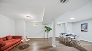 Un salon moderne avec un canapé rouge, une petite table, un coin repas avec une table bleue et des chaises blanches, et une plante en pot.