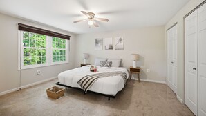 Une chambre à coucher comprenant un lit, un ventilateur de plafond, une fenêtre, une table de chevet, une lampe et un placard.