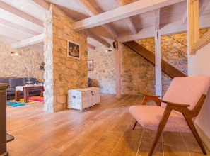 Un intérieur rustique avec des murs en pierre, un plafond en bois, un escalier, un canapé, une table et une chaise.