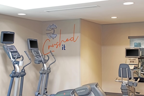 An indoor gym with elliptical machines, a wall with motivational text, and a treadmill.